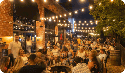 people sit at tables outside under string lights